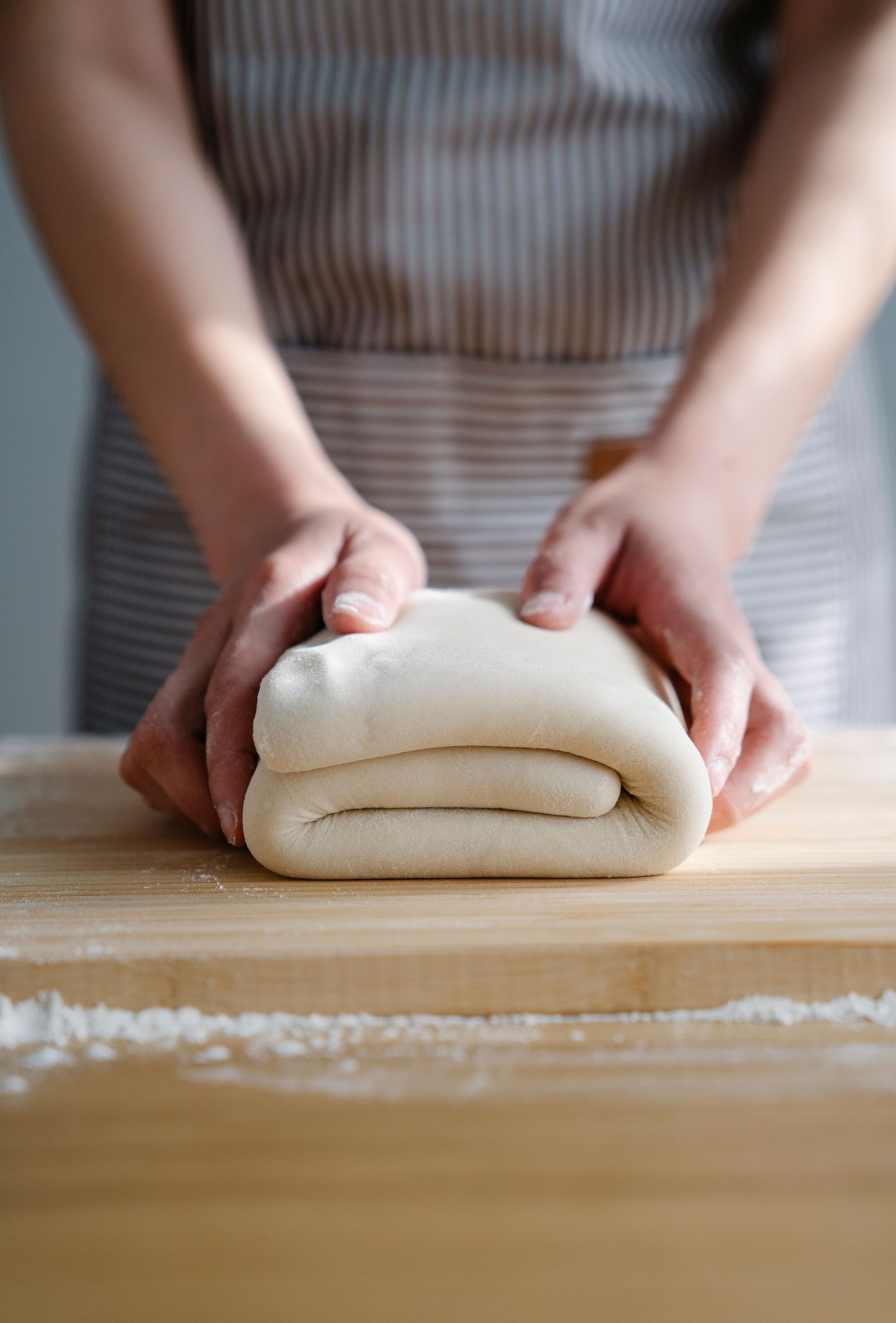 Hands folding a thick sheet of dough on a wooden worktop.